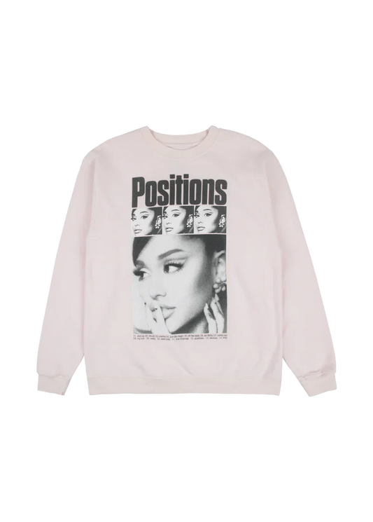 Light pink crewneck sweatshirt featuring a collage-style black-and-white print of Ariana Grande’s face repeated above the bold “Positions” title, with the full tracklist from the album printed beneath.

